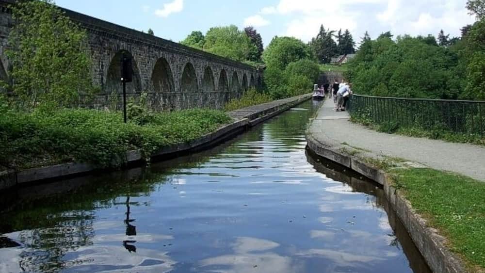Un canal surmonté d’un pont en pierre, bordé de verdure et doté d’un sentier.