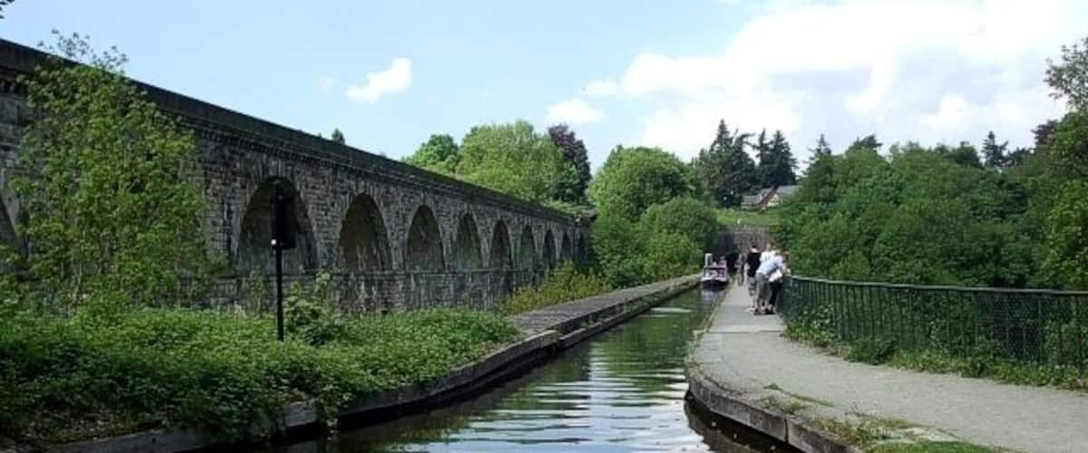 A canal with a stone bridge, greenery, and a pathway.