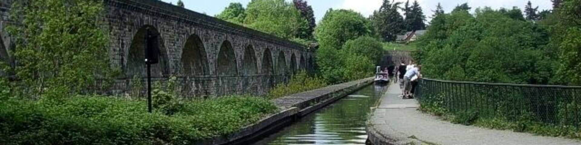 A canal with a stone bridge, greenery, and a pathway.