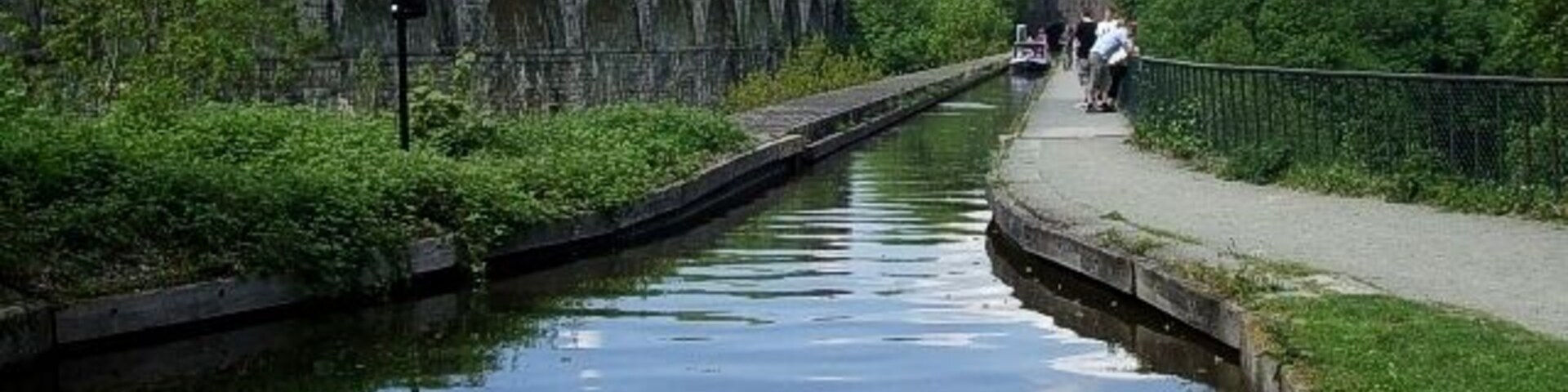 Un canal con un puente de piedra, vegetación y un sendero.
