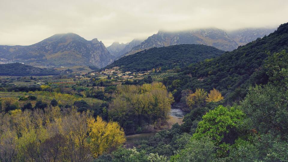 A mountainous landscape with a village nestled among the hills, a river flowing through the valley, and dense forested areas.
