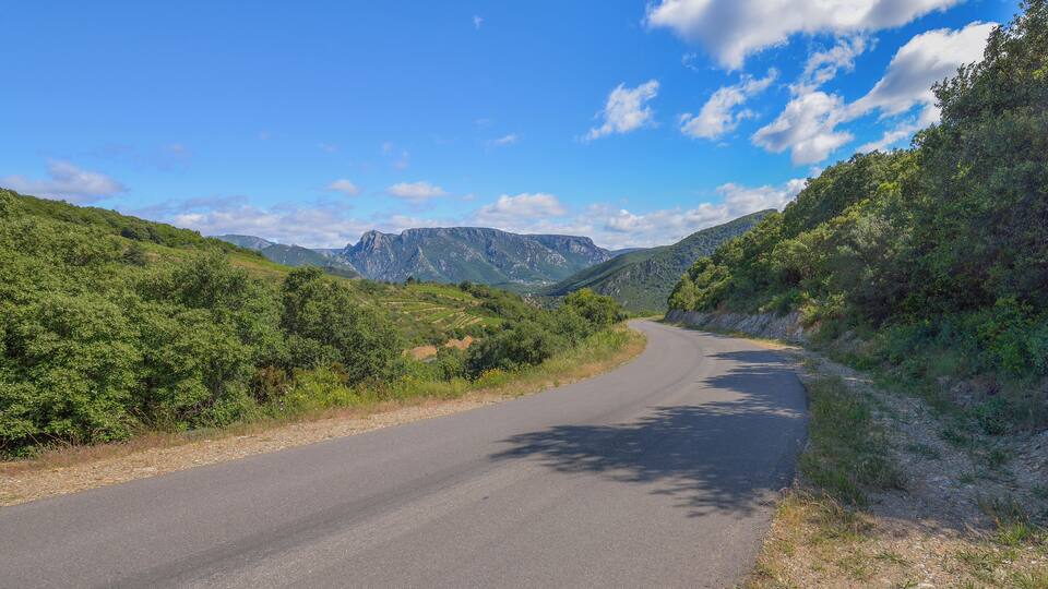 A winding road through a mountainous landscape with lush greenery and rocky cliffs.