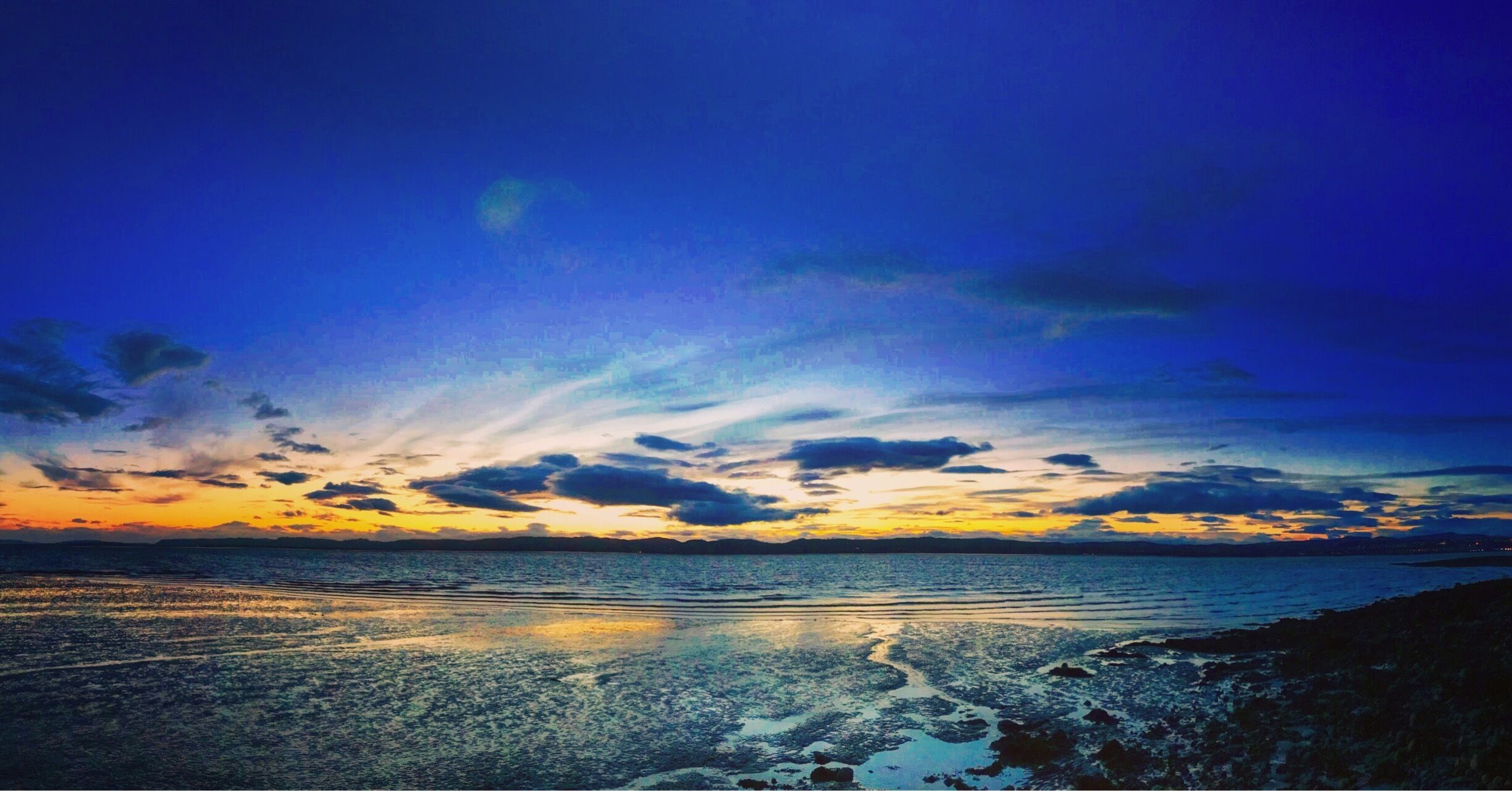 A sunset over a calm sea with a rocky shoreline.