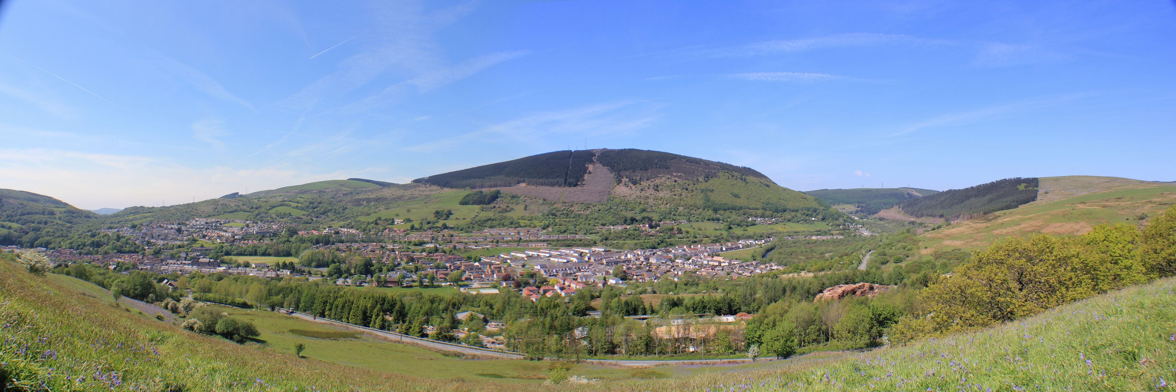 A town nestled in a valley with rolling hills and a prominent mountain in the background.