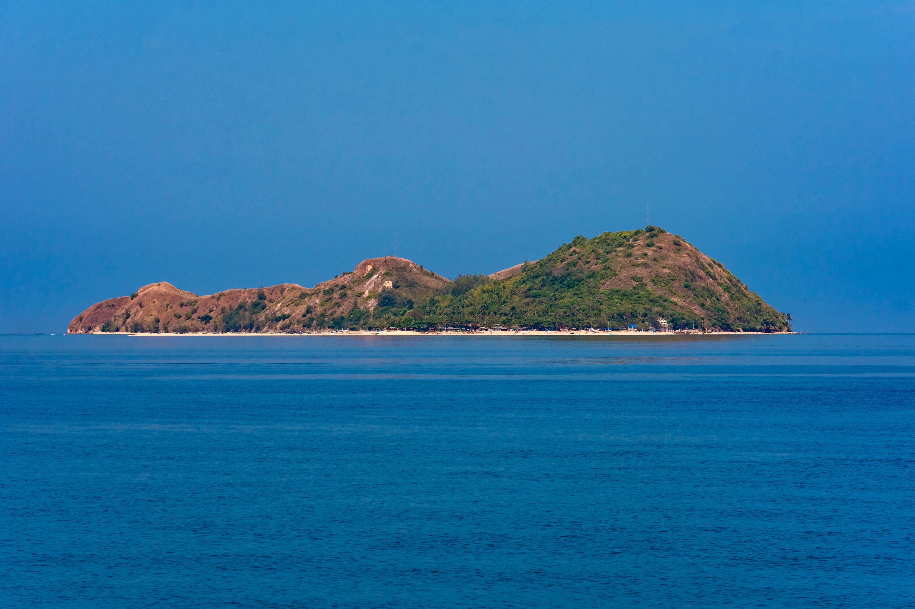 A small island with a clear blue sea and a few buildings on the shore.