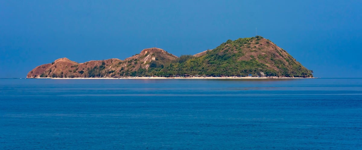 A small island with a clear blue sea and a few buildings on the shore.