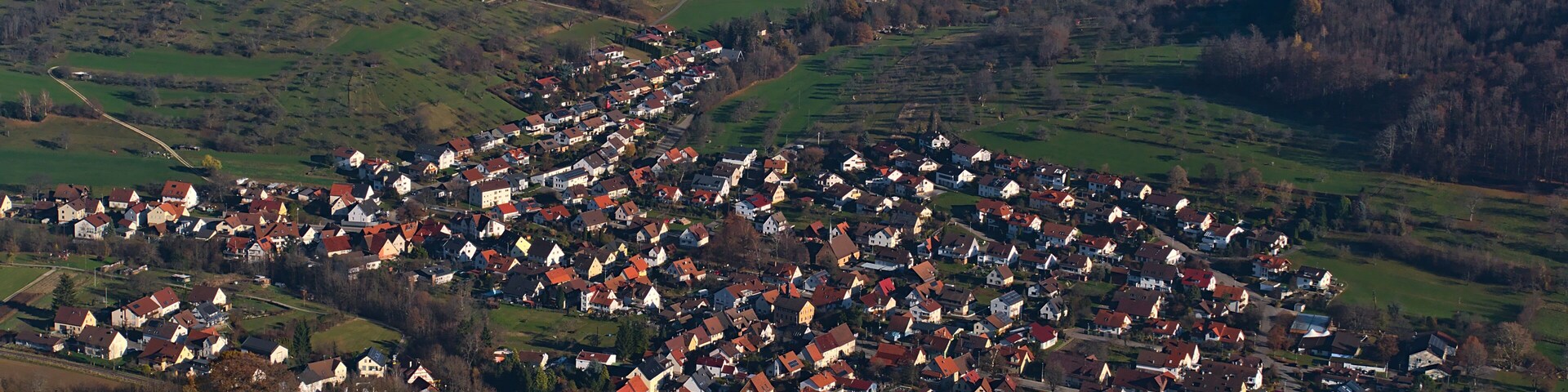 Un pueblo rural con casas agrupadas en una ladera, rodeado de campos verdes y colinas boscosas.