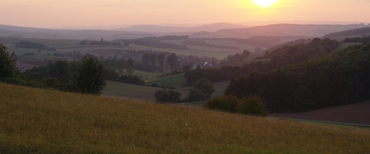 A sunset over rolling hills with a road cutting through the landscape.