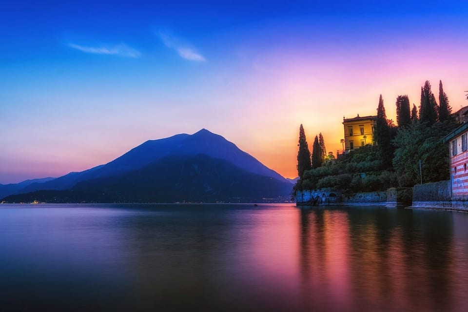A mountain at sunset, a calm lake, and a building with red and white stripes.
