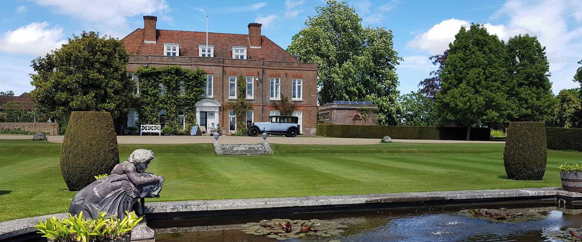 A large brick house with a lawn, a pond with lily pads, and a statue.