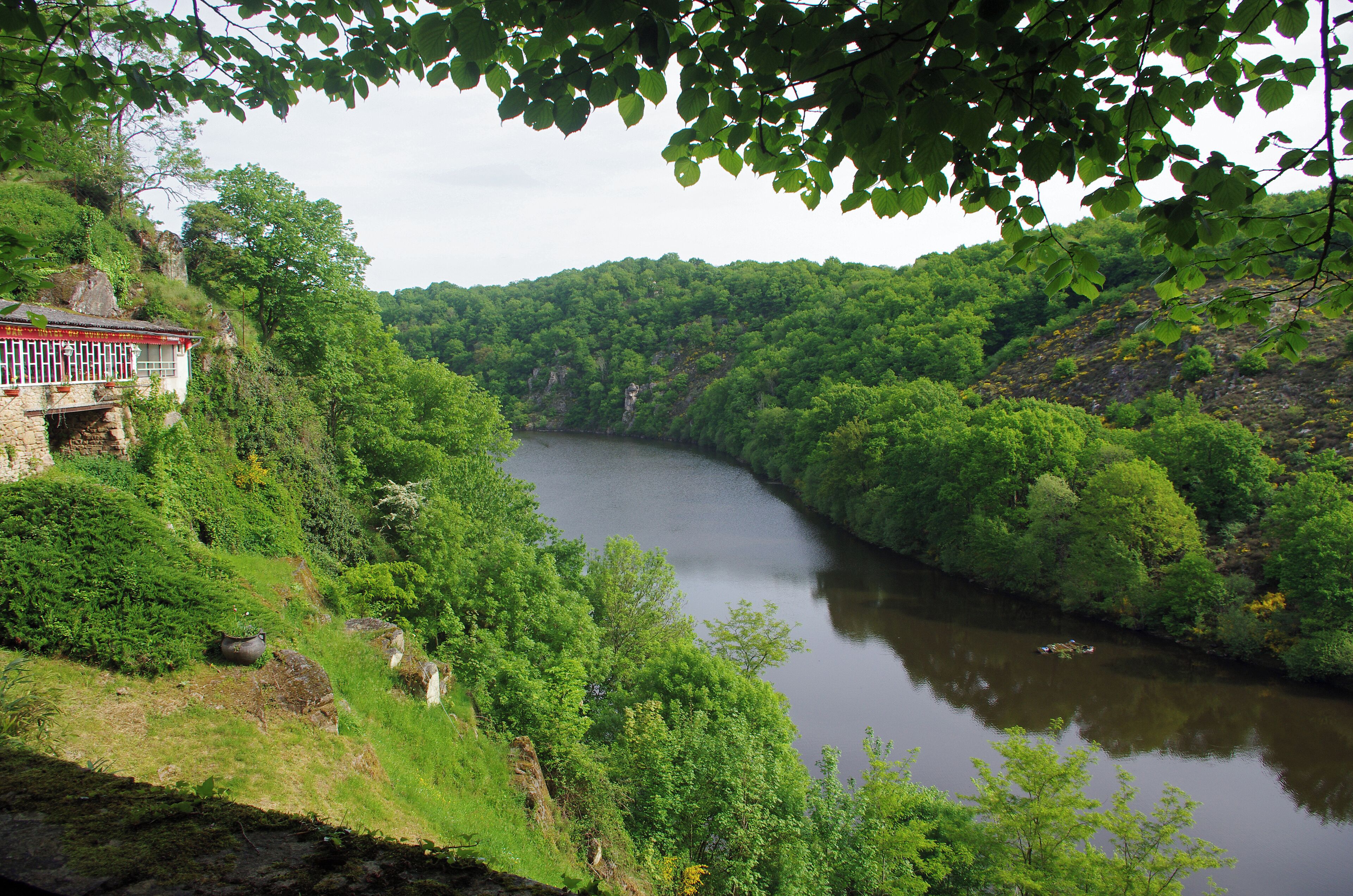 A river surrounded by lush greenery and a traditional building on a hillside.