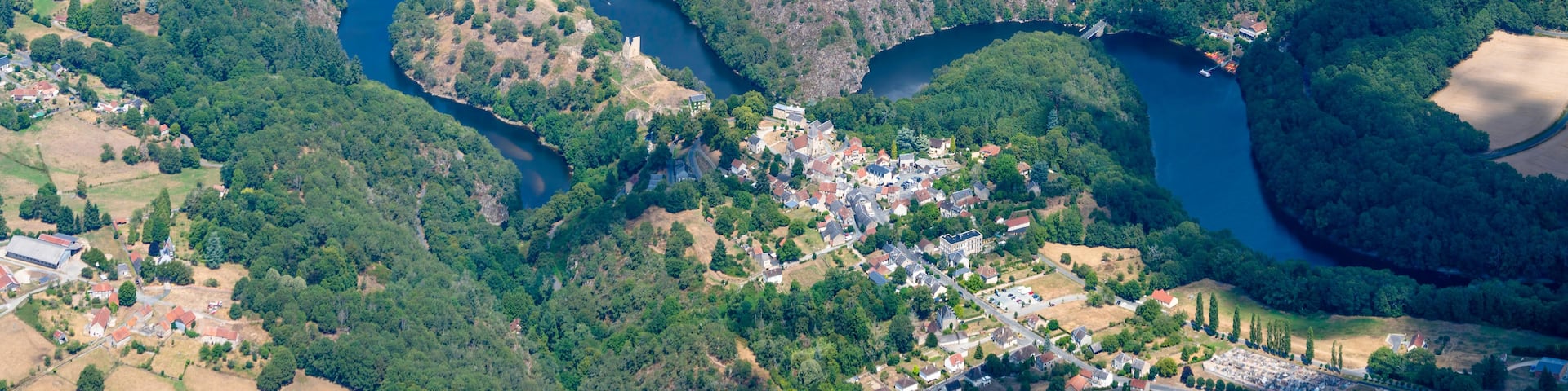 An aerial view of a town nestled between two rivers, surrounded by dense forests and fields.