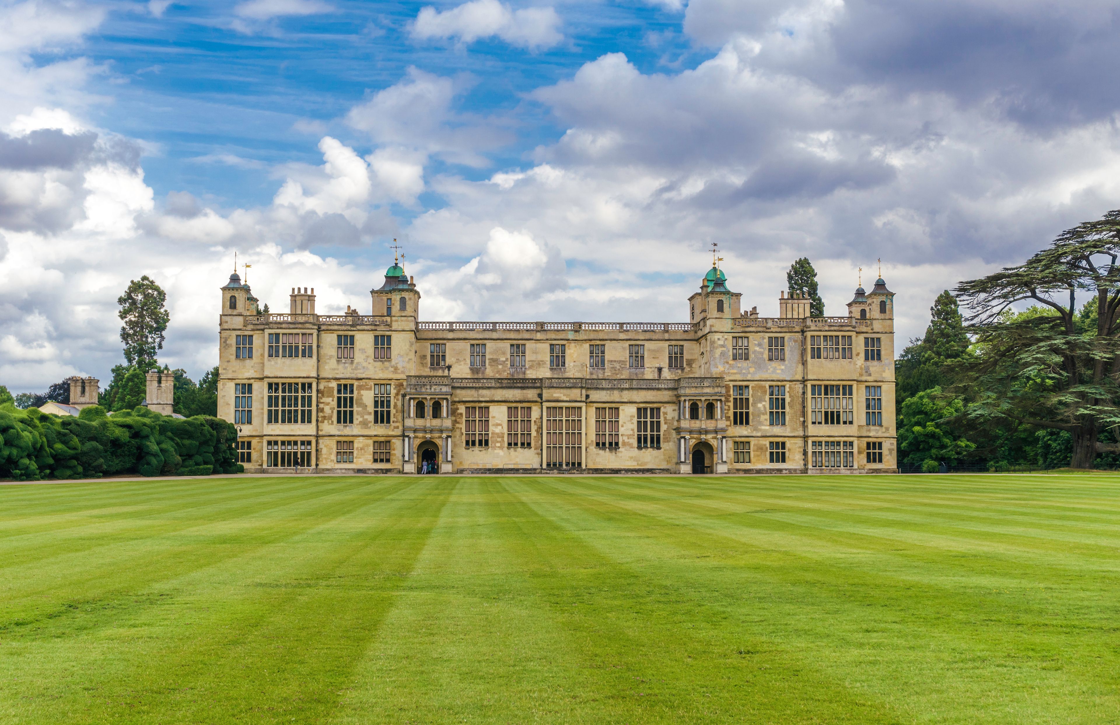 A large, historic building with multiple towers and a well-maintained lawn in front.