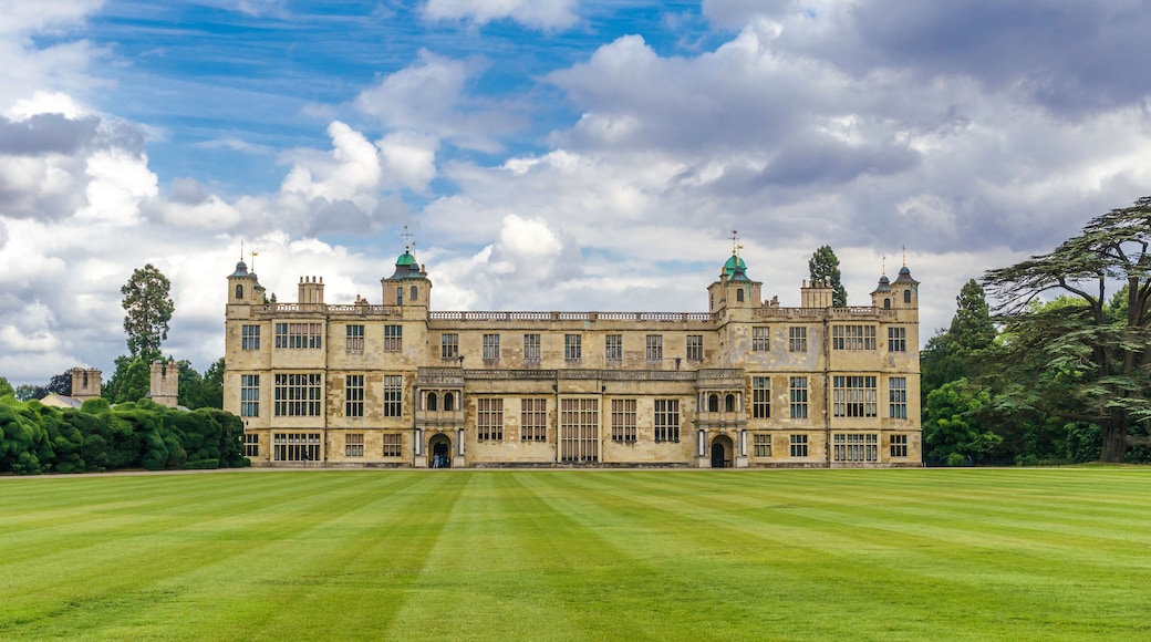 A large, historic building with multiple towers and a well-maintained lawn in front.
