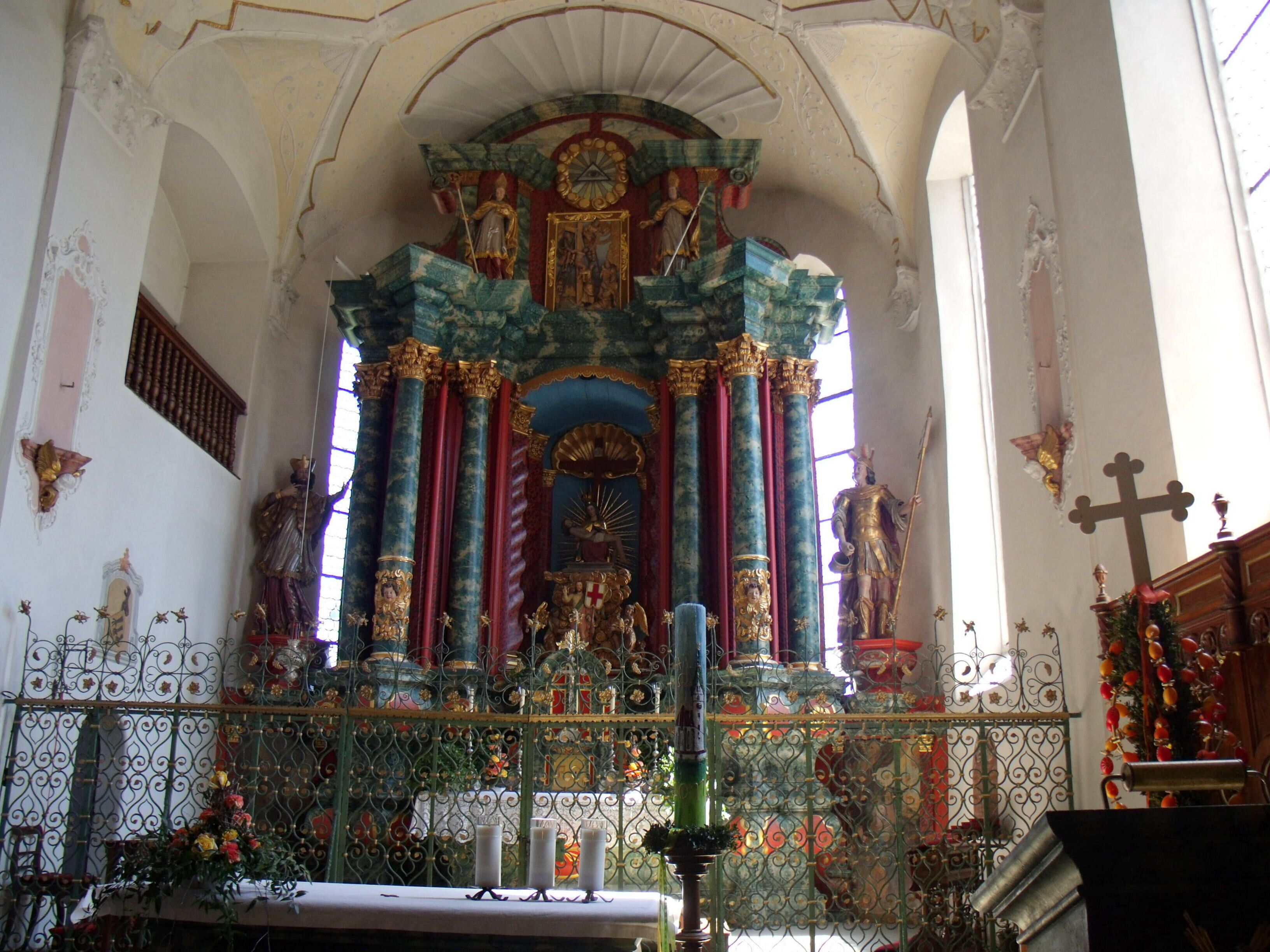 An ornate church interior with a high altar, religious statues, and a large crucifix.