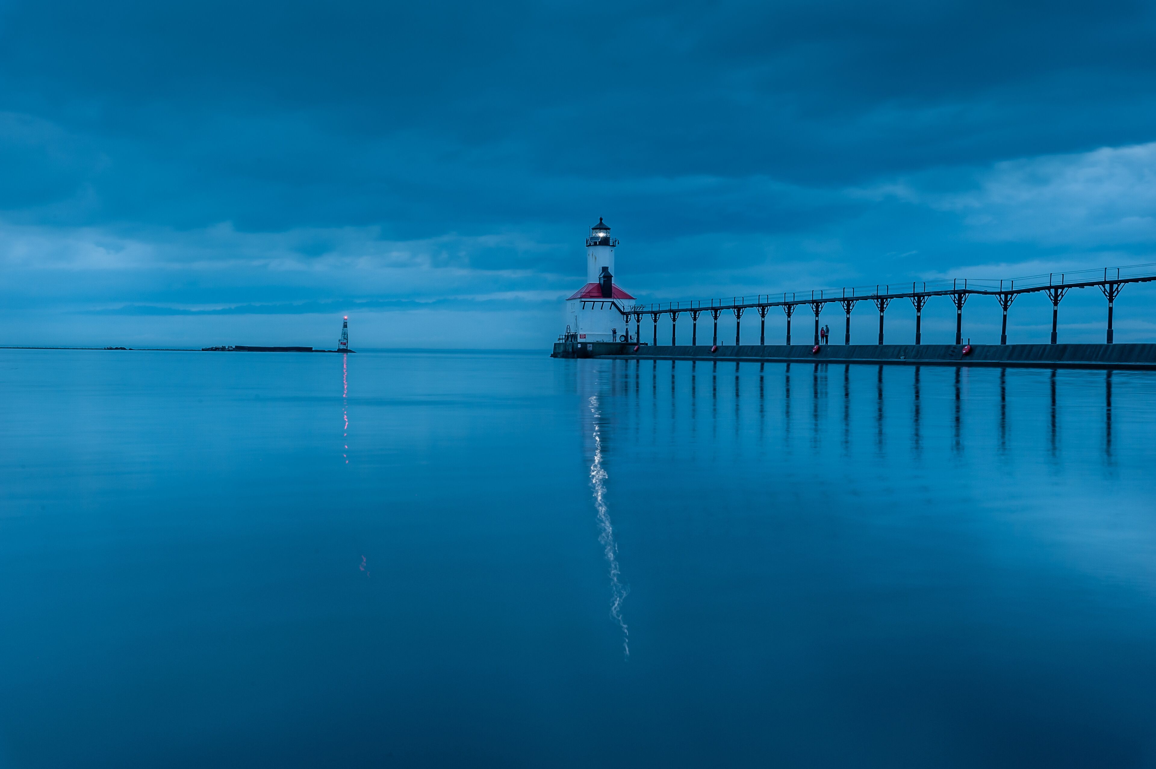 still water long exposure image of stormclouds pier and lighthouse at michigan city indiana