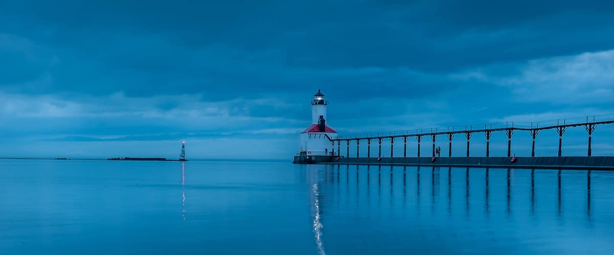 still water long exposure image of stormclouds pier and lighthouse at michigan city indiana