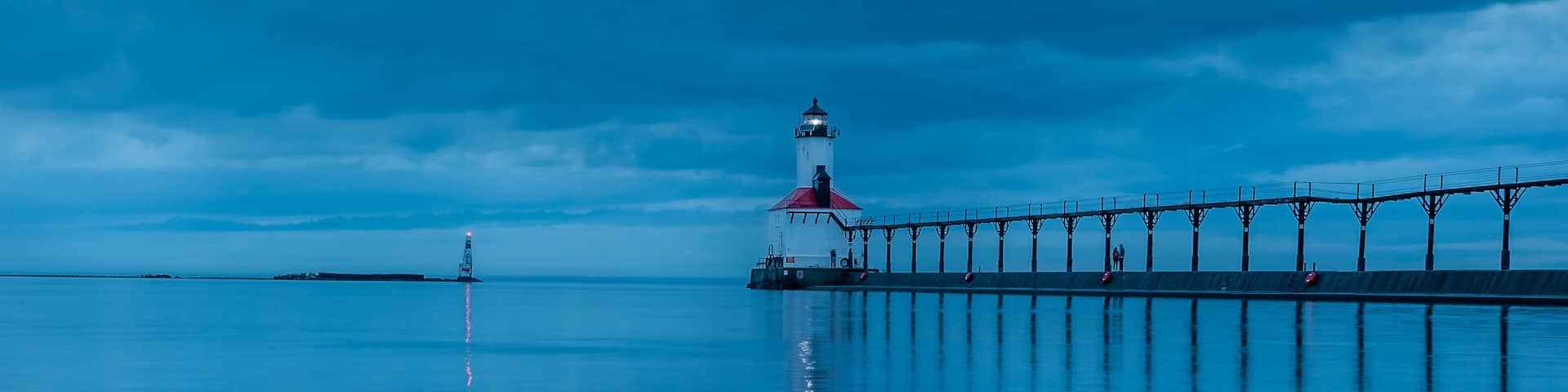 still water long exposure image of stormclouds pier and lighthouse at michigan city indiana