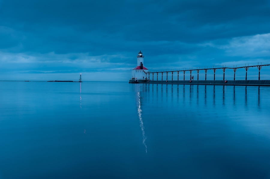 still water long exposure image of stormclouds pier and lighthouse at michigan city indiana
