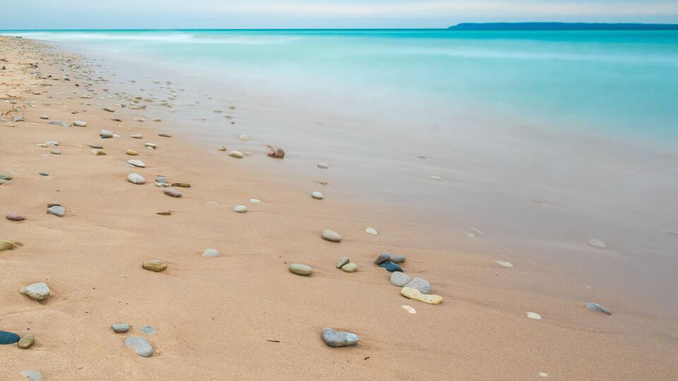 A sandy beach with scattered rocks and calm turquoise waters under a clear sky.