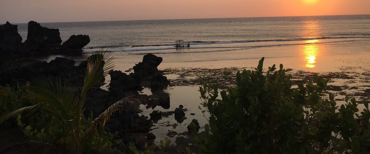 A sunset over a rocky beach with calm waves and a clear sky.