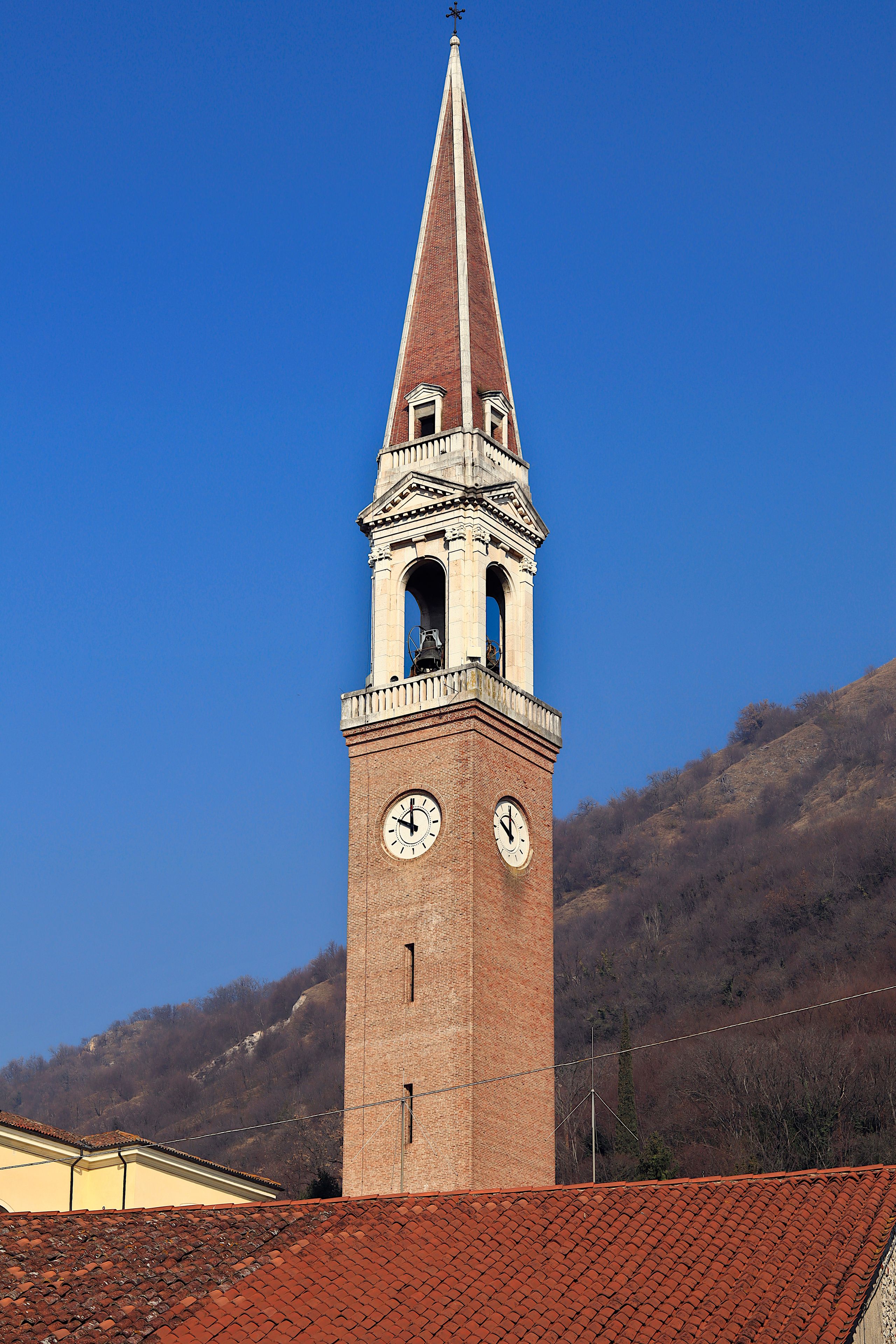 A tall brick tower with a clock and a spire against a clear blue sky.