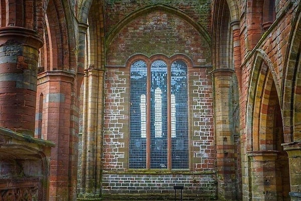 An interior of a historic building with arched brick walls and a large stained glass window.