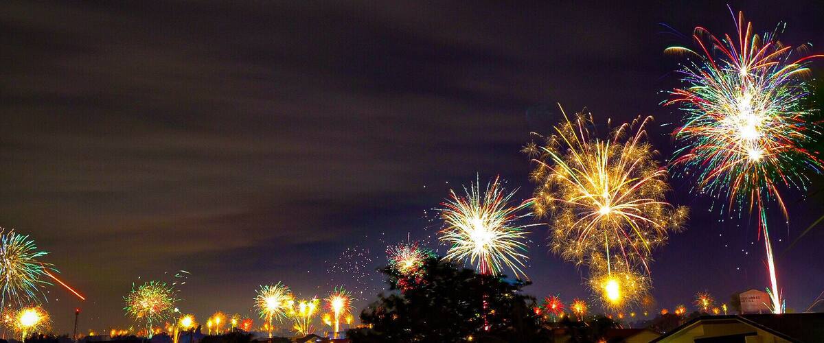 A night sky with multiple fireworks displays over a residential area.