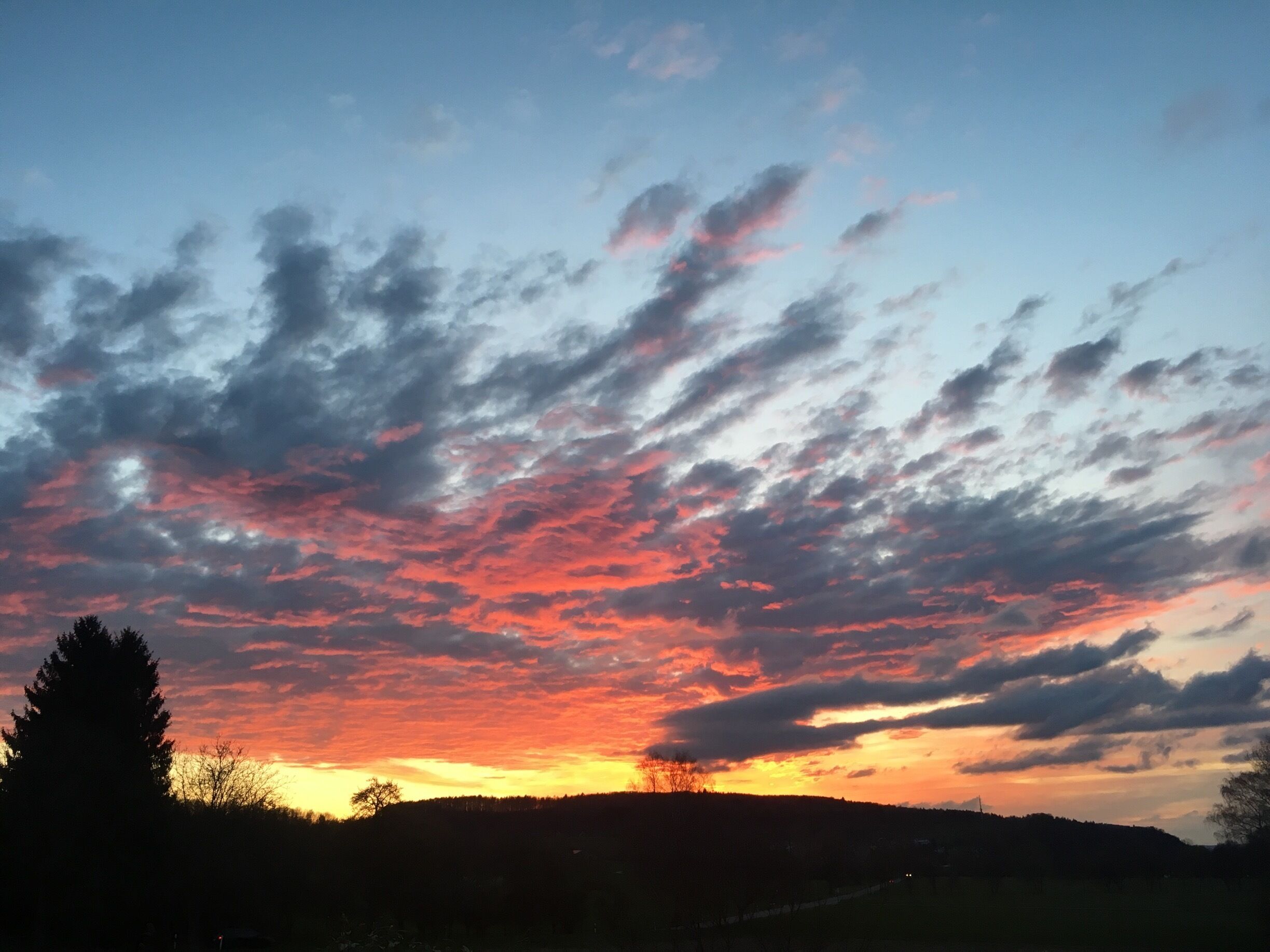 A sunset over a hilly landscape with scattered clouds.