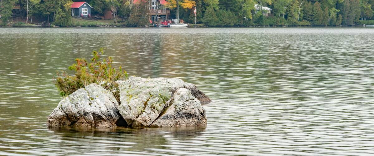 A lake with a house on the shore, surrounded by autumn-colored trees.