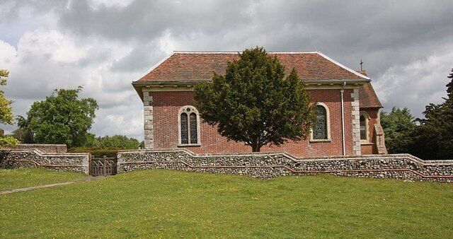 A brick church with a stone wall and a large tree in front.