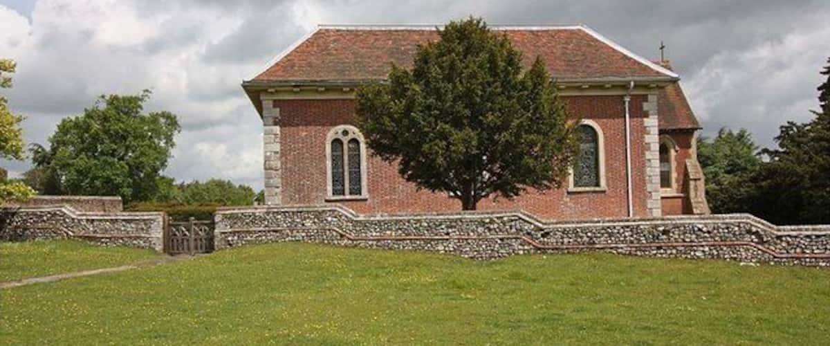 A brick church with a stone wall and a large tree in front.