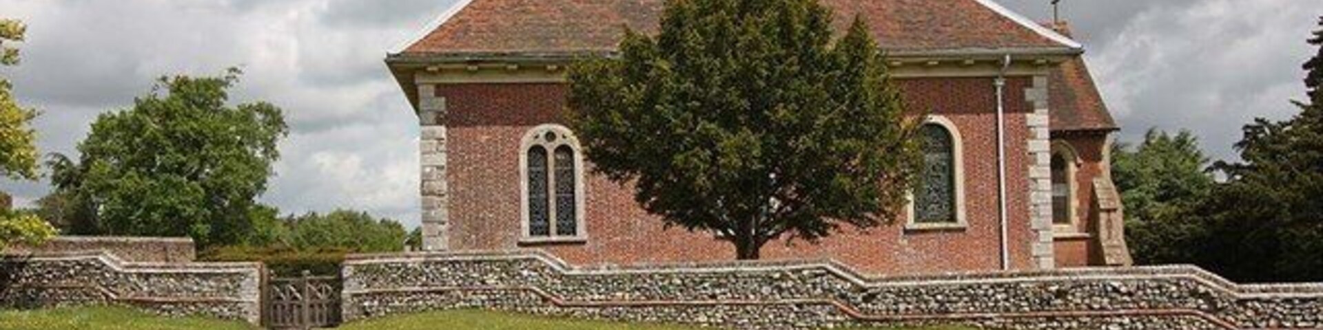 A brick church with a stone wall and a large tree in front.