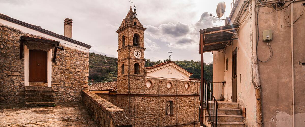 A stone church with a bell tower and a clock, a cobblestone street, and a rustic building with a wooden door.
