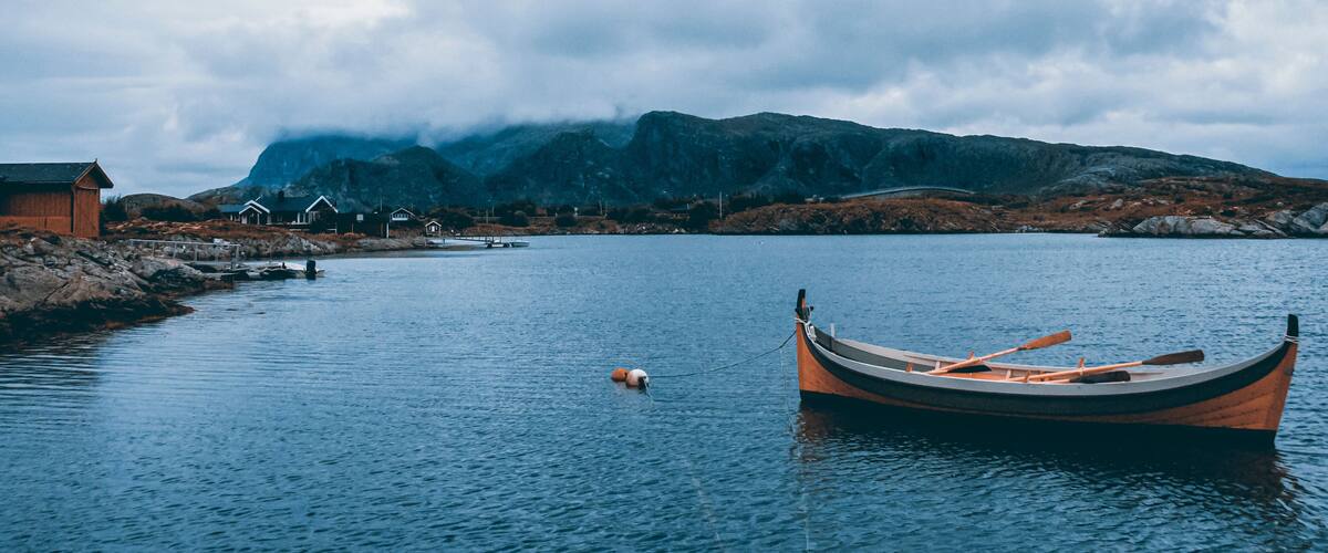 A wooden boat on calm water, a small buoy, and a cluster of houses near a mountain.