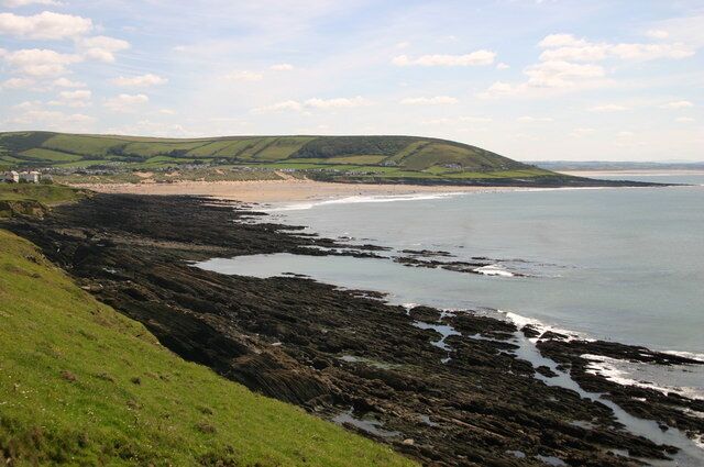 A coastal landscape with a rocky shoreline, green hills, and a beach.