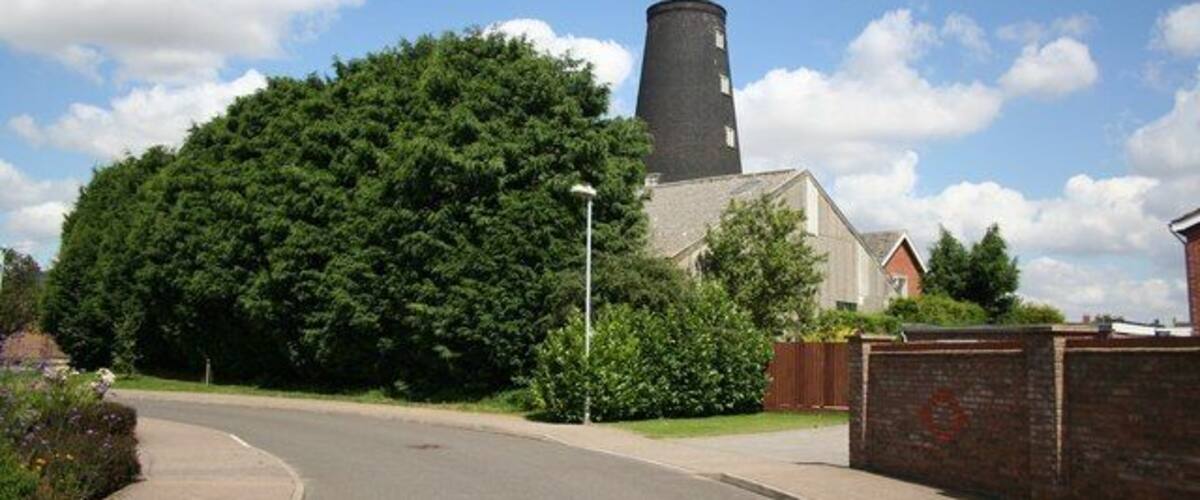 A church with a tall tower, surrounded by trees and a paved road.