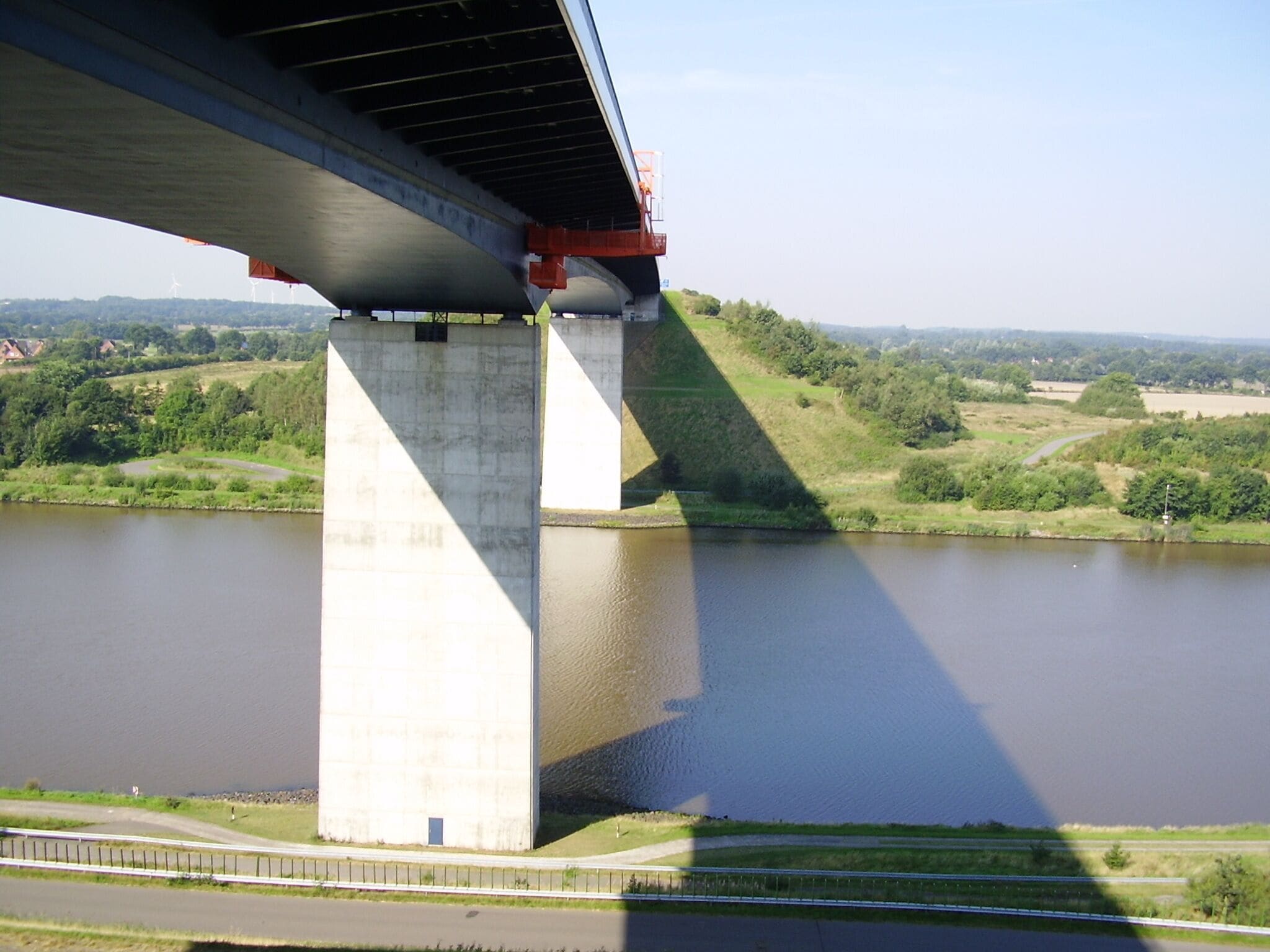 A concrete bridge over a river with green hills in the background.