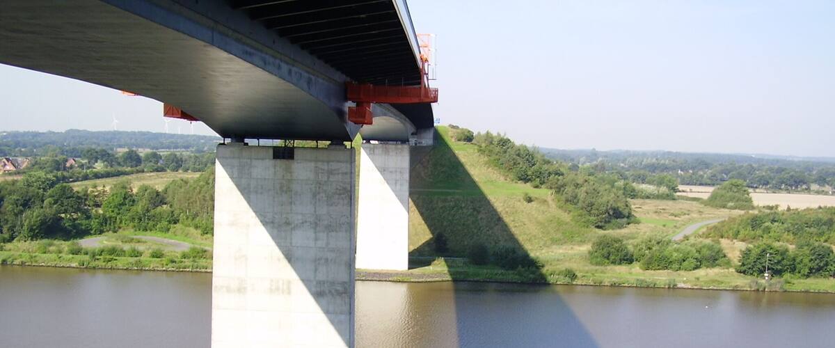 A concrete bridge over a river with green hills in the background.
