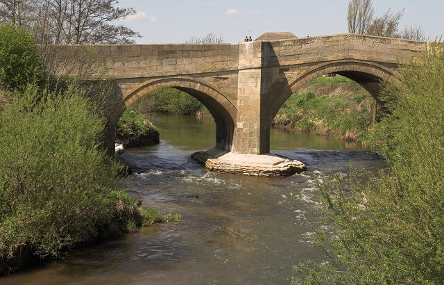 A stone bridge over a river with greenery on either side.