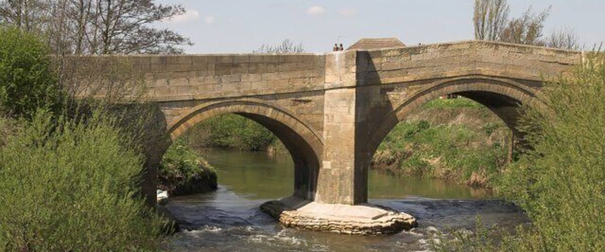 A stone bridge over a river with greenery on either side.