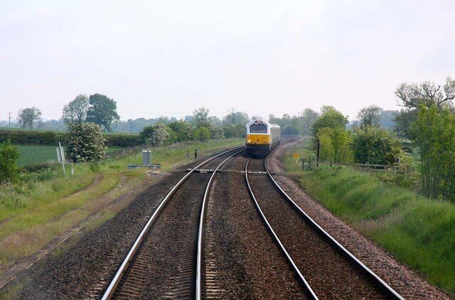 A train on railway tracks in a rural area with greenery and trees.
