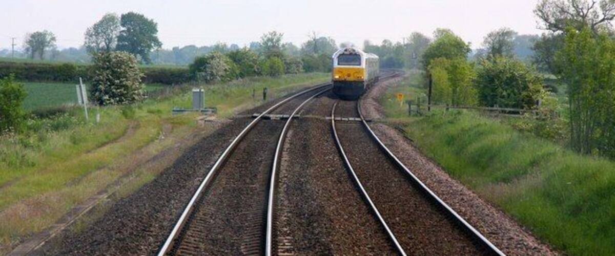 A train on railway tracks in a rural area with greenery and trees.