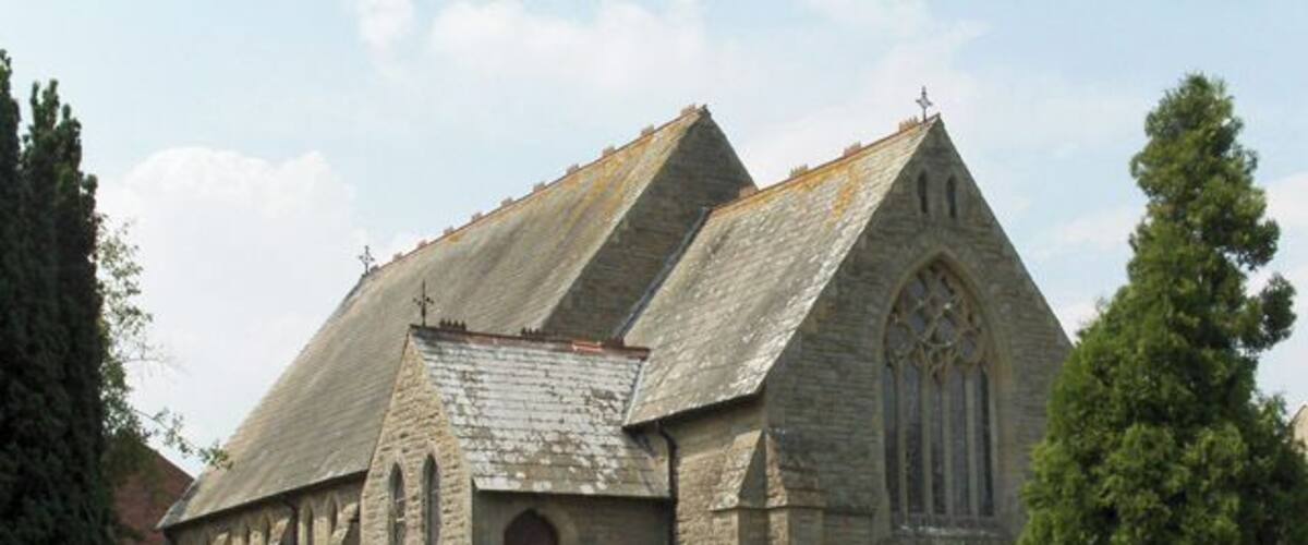 A stone church with a pointed roof and arched windows, surrounded by a cemetery with headstones.