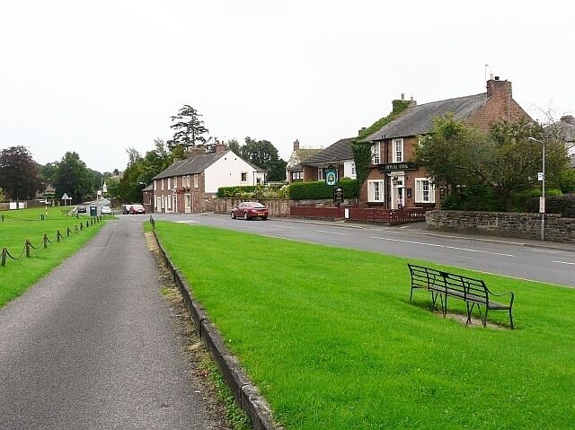 A rural street with a pub, a grassy area, and a bench.
