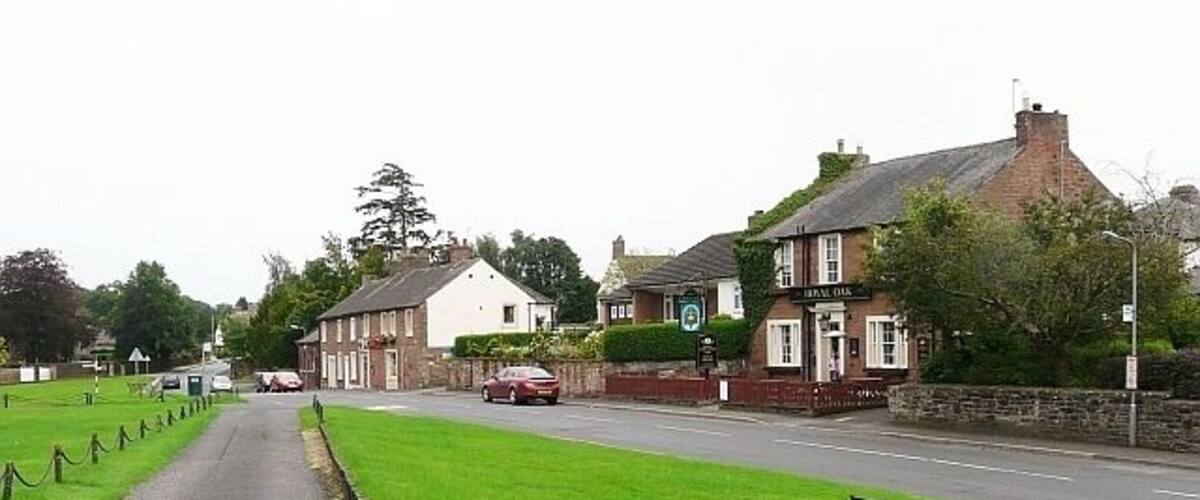 A rural street with a pub, a grassy area, and a bench.