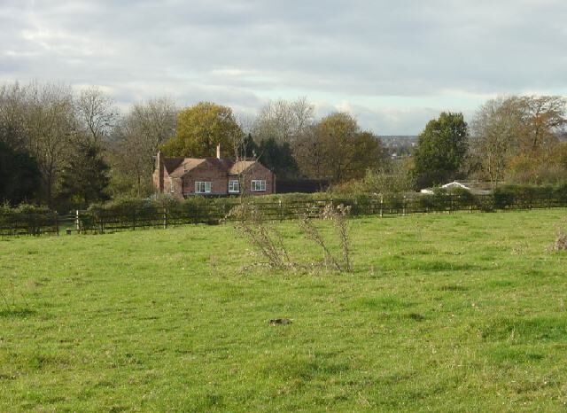 A rural landscape with a house, green field, and trees.