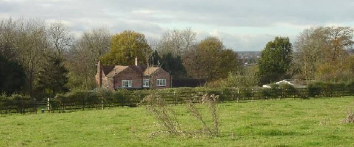 A rural landscape with a house, green field, and trees.