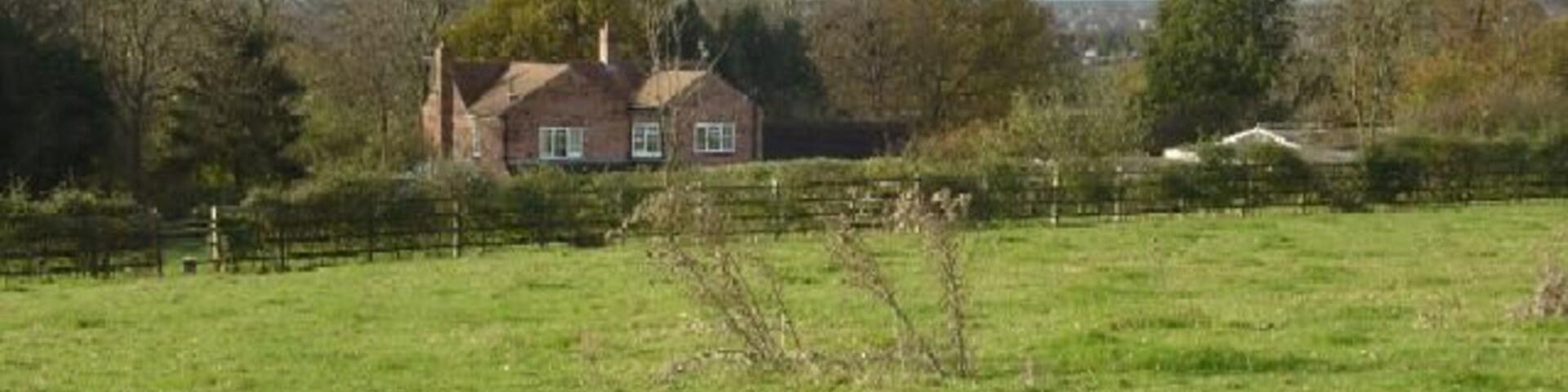 A rural landscape with a house, green field, and trees.