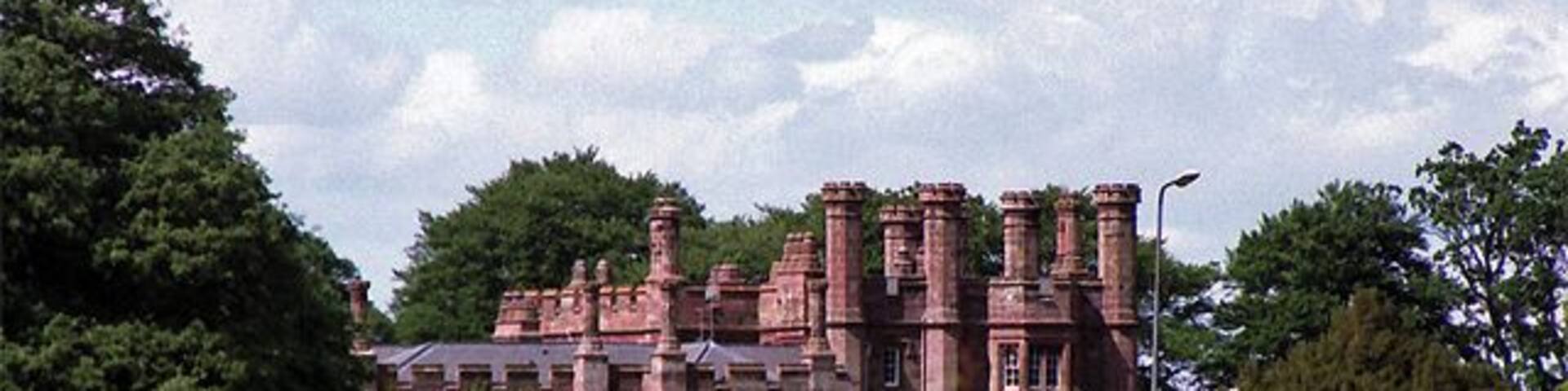 A large, historic building with multiple chimneys and surrounded by lush greenery.